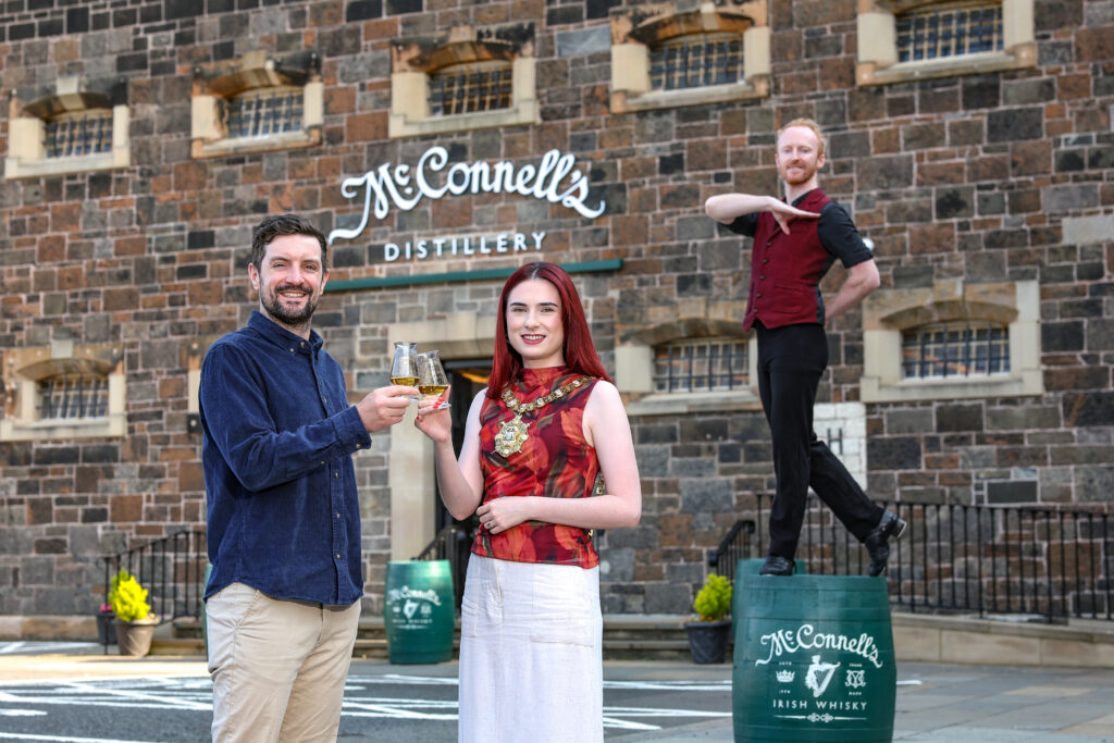 Belfast Lord Mayor and Irish Language guide, Cormac raise a glass, while Unity Dance's Kevin poses on top of a barrel outside McConnell's Distillery.